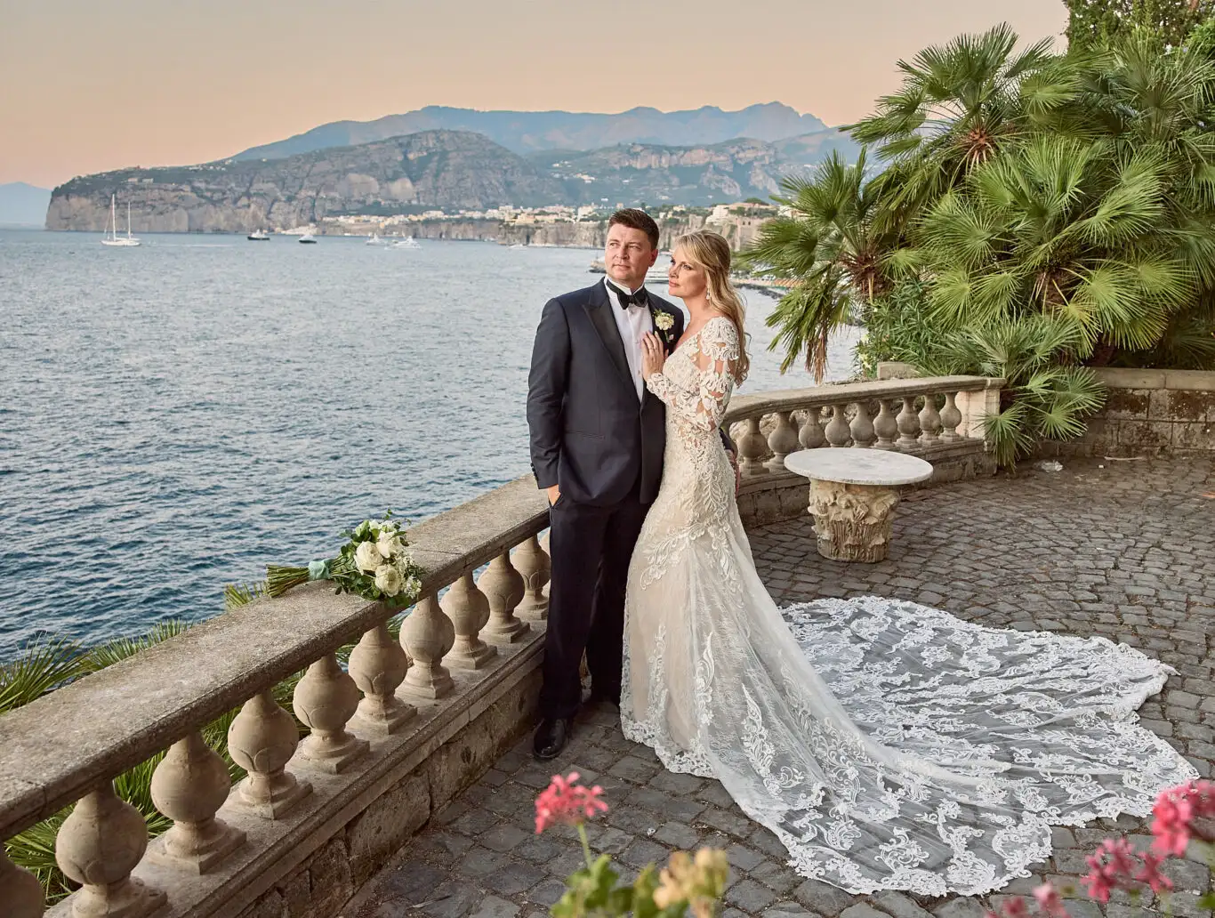Bride and groom on a seaside terrace in Sorrento at sunset, with the bay and cliffs behind them