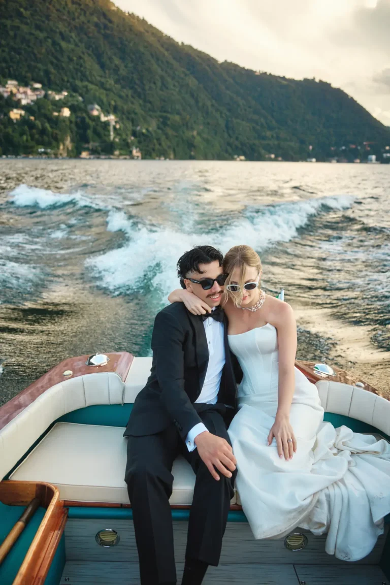Bride and groom in sunglasses sitting at the back of a boat on Lake Como, returning to Villa Noseda